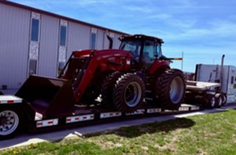 White Semi truck hauling a red tractor loader