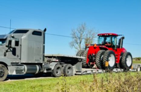 A gray sleeper truck carrying a Case IH Tractor on a flatbed trailer