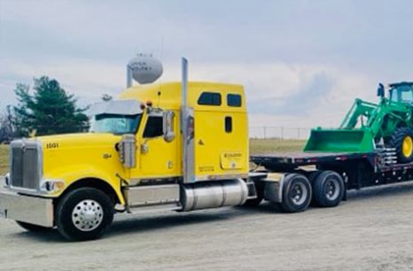 Two John Deere tractor loaders being hauled on a flatbed