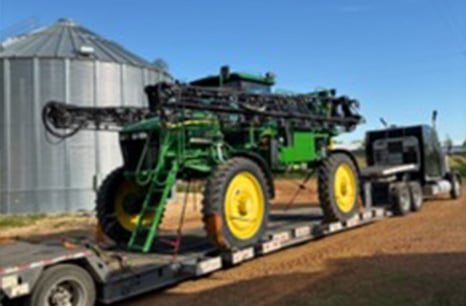 Semi truck carrying John Deere sprayer on a flatbed trailer