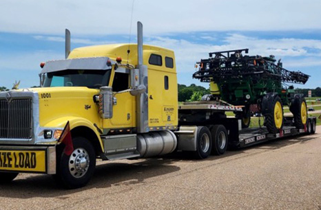 Yellow Semi truck hauling a John Deere sprayer