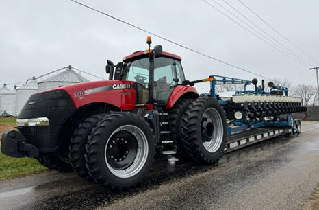 Case IH 340 tractir carrying a blue planter on a flatbed trailer 