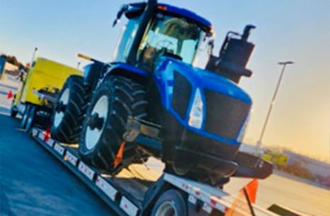 New Hollad Tractor being hualed on a flat bed trailer
